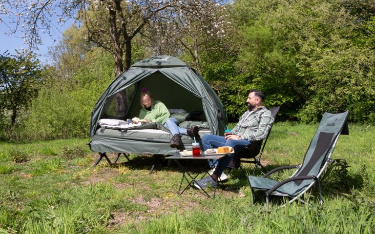 Zeltliege Haug in army green mit zwei Personen, dem Campingtisch Ruka und zwei Campingstühlen in der Natur