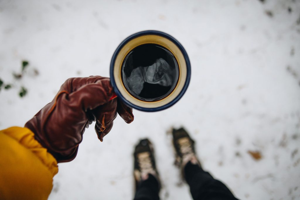 Person mit Handschuhen und Kaffeetasse im Schnee