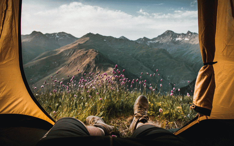 Blick aus Zelt auf Wanderstiefel, lilafarbene Blumen und Bergkulisse