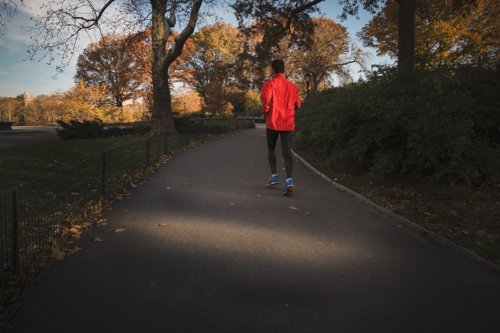 Mann der nach Erkältung Sport macht und durch einen Park joggt