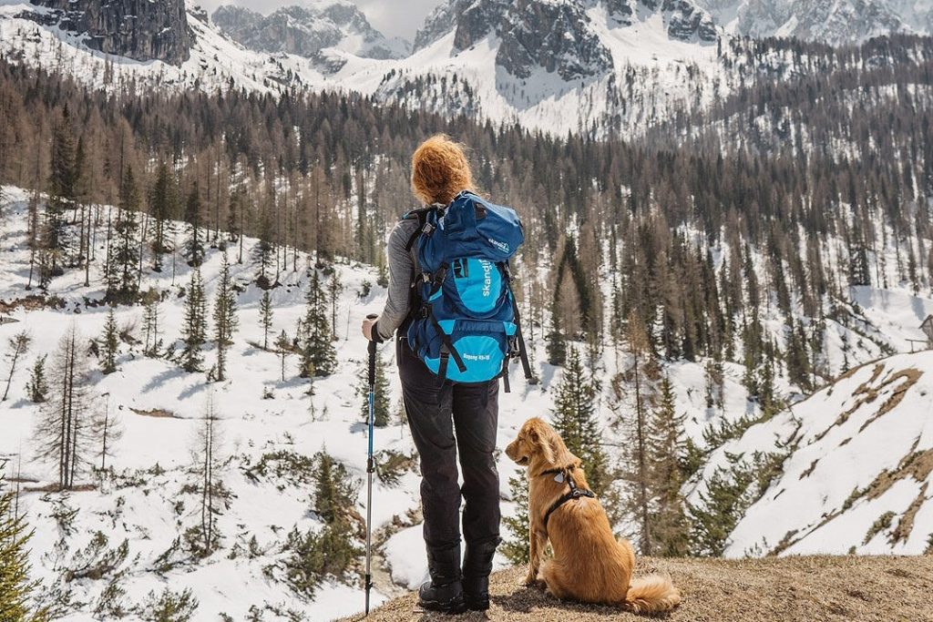 Frau mit Skandika Rucksack und Hund mit Blick auf die schneebedeckten Berge