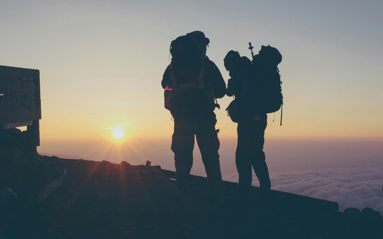 Silhouette von zwei Wanderern beim Sonnenaufgang auf einem Berg